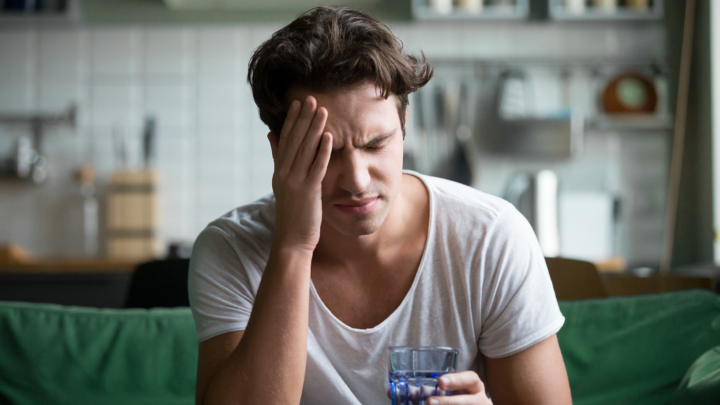 Man with headache sitting on edge of bed, suffering from hangover. IV therapy as a hangover cure is discussed in this blog post by Cutler Integrative Medicine in Bloomfield Hills, Michigan.